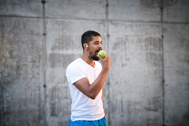 Attraente giovane sportivo che mangia frutta fresca di mela verde dopo l'allenamento promuovendo uno stile di vita sano e la dieta