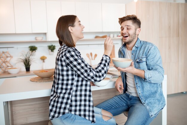 Attraente giovane uomo felice e donna in cucina, fare colazione, coppia insieme al mattino, sorridendo