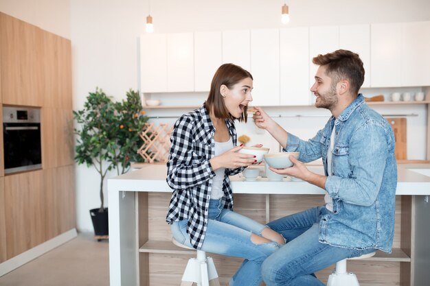 Attraente giovane uomo felice e donna in cucina, fare colazione, coppia insieme al mattino, sorridendo