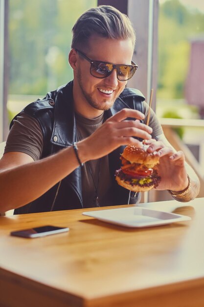 Attraente hipster vestito con una giacca di pelle che mangia un hamburger vegano.