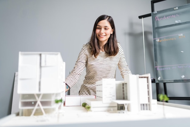 Attraente ingegnere sorridente guardando il modello architettonico sul posto di lavoro