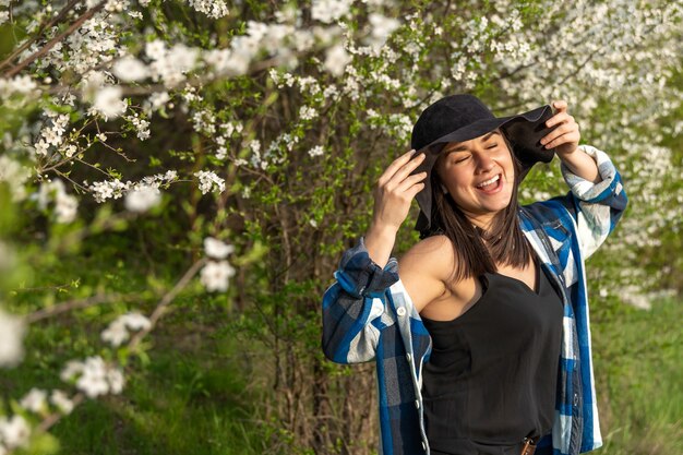 Attraente ragazza allegra con un cappello tra gli alberi in fiore in primavera, in uno stile casual.