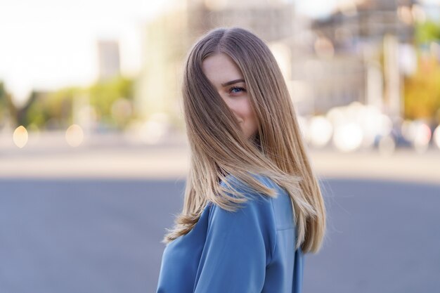 Attraente ragazza bionda allegra con capelli lunghi volanti sorridente che ride in città