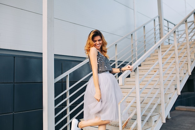 Attraente ragazza bionda in gonna di tulle divertendosi sulle scale. Sta sorridendo.