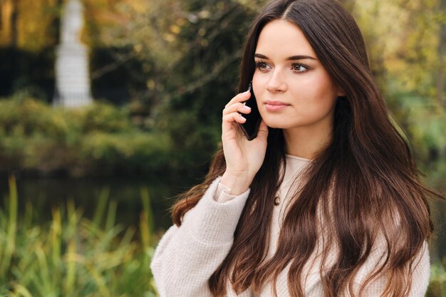 Attraente ragazza bruna distoglie lo sguardo premurosamente parlando sul cellulare nel bellissimo parco cittadino