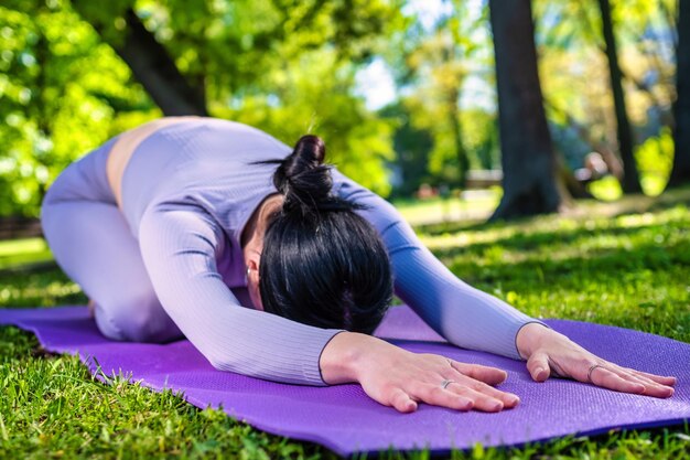 Attraente ragazza con lunghi capelli neri vestita di viola facendo yoga posa La posa del bambino