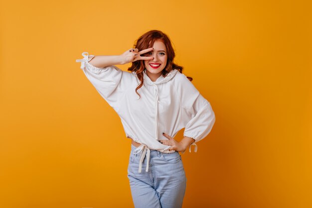 Attraente ragazza sottile in maglione oversize che esprime felicità. Donna di zenzero di buon umore che balla sulla parete gialla.