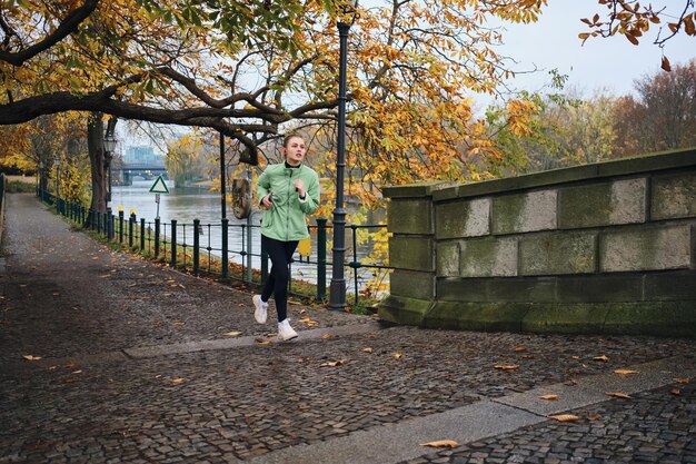 Attraente ragazza sportiva che corre sognante nell'accogliente parco cittadino autunnale