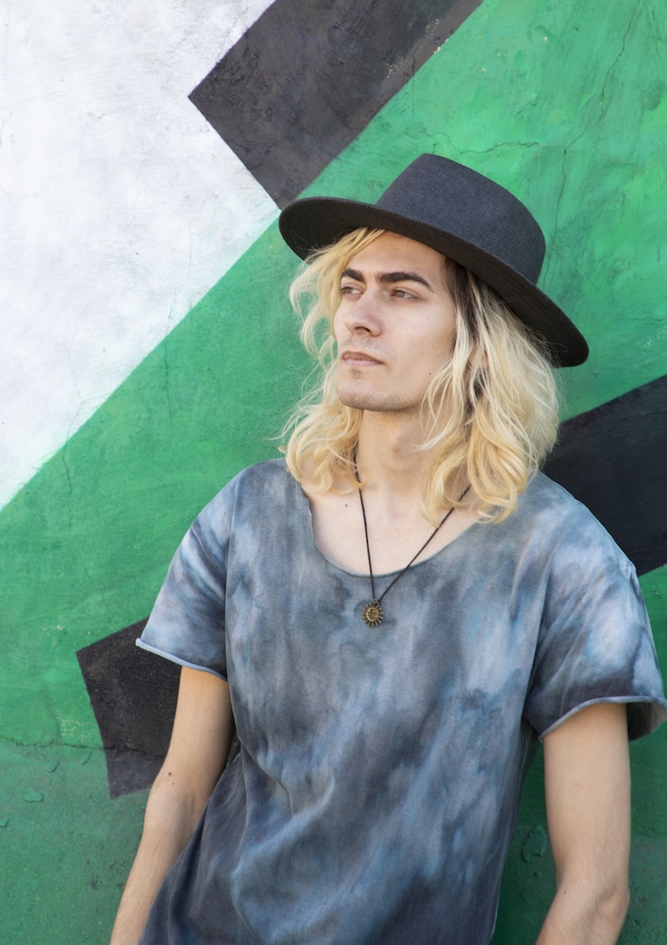 Foto gratuito attraente ragazzo armeno con un cappello appoggiato su un muro blu e verde e guardando lontano