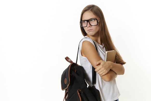Attraente studentessa universitaria frustrata che trasporta zaino e libro di testo, arrabbiata per gli esami falliti, molti compiti