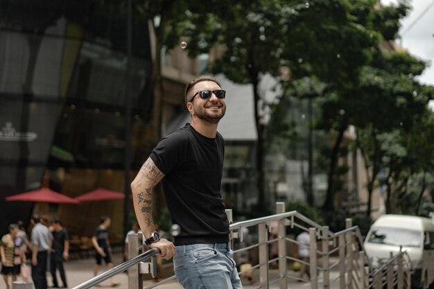 Attraente uomo tatuato felice sorridente per strada a Kuala Lumpur. Uomini urbani, stile di abbigliamento. Le bolle di sapone volano nell'aria.