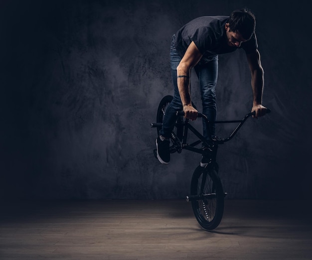 Сaucasian uomo, fa una figura acrobatica con BMX in uno studio. Isolato su uno sfondo scuro.