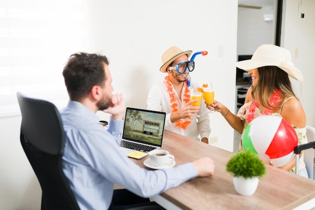 Auguri per la nostra vacanza! Felice giovane uomo e donna che indossano abiti tropicali che fanno un brindisi con le mimose dopo aver prenotato un viaggio in spiaggia presso l'agenzia di viaggi