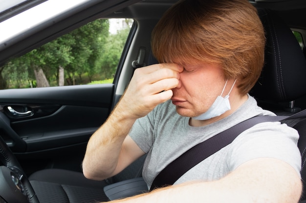 Autista di automobile esaurito sonnolento che toglie maschera medica