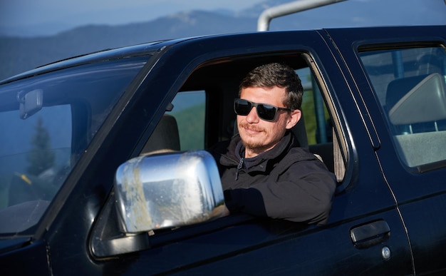 Autista maschio con occhiali da sole seduto nella cabina di un'auto nera