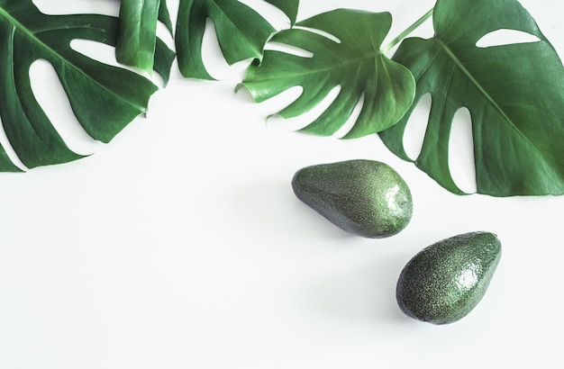 Avocado con foglie tropicali su sfondo bianco