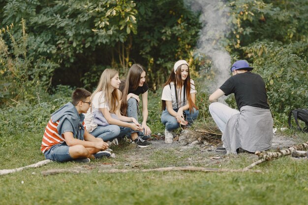 Avventura, viaggi, turismo, escursione e concetto di persone. Gruppo di amici sorridenti in una foresta. Persone sedute vicino al falò.