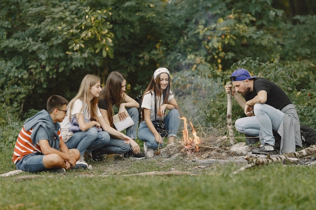 Avventura, viaggi, turismo, escursione e concetto di persone. Gruppo di amici sorridenti in una foresta. Persone sedute vicino al falò.