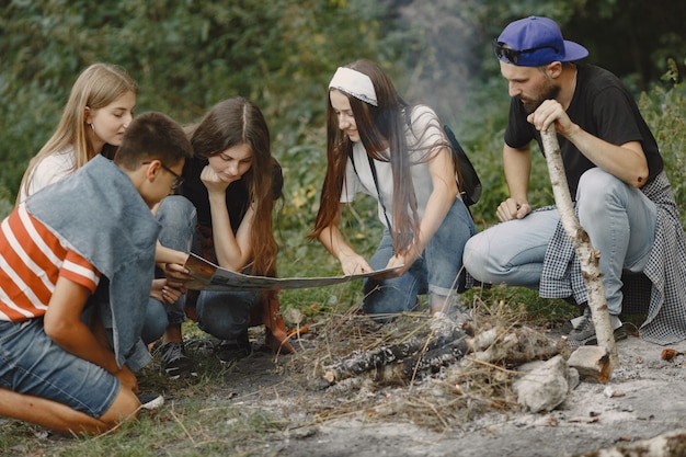 Avventura, viaggi, turismo, escursione e concetto di persone. Gruppo di amici sorridenti in una foresta. Persone sedute vicino al falò.