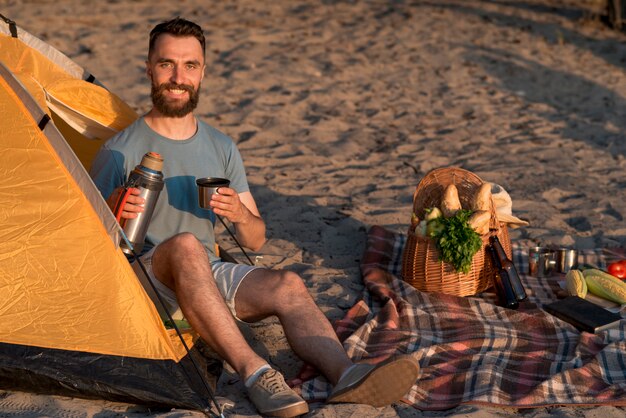 Avventuriero che esamina la macchina fotografica che tiene un thermos