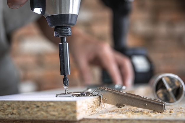 Avvitare una vite autofilettante in un foro di fissaggio metallico su un listello di legno usando un cacciavite, opera di un falegname.