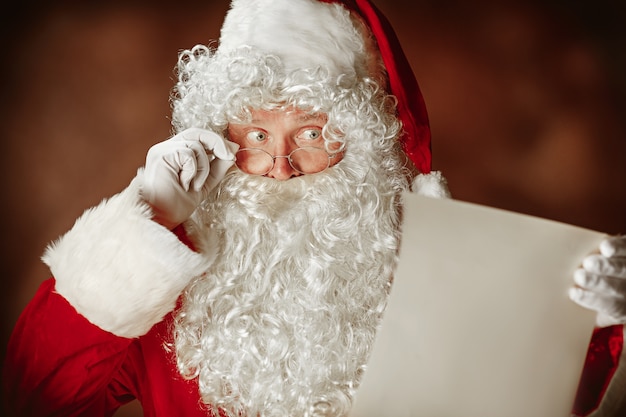 Babbo Natale con una lussuosa barba bianca, cappello di Babbo Natale e una lettera di lettura in costume rosso