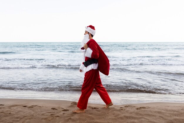 Babbo Natale di vista laterale che cammina sulla spiaggia