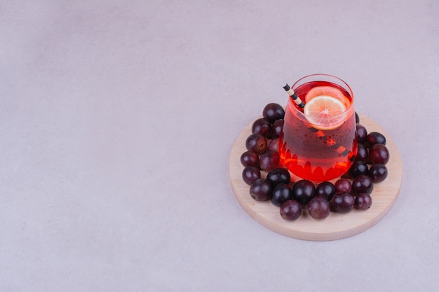 Bacche di ciliegia rossa con un bicchiere di succo su grigio.