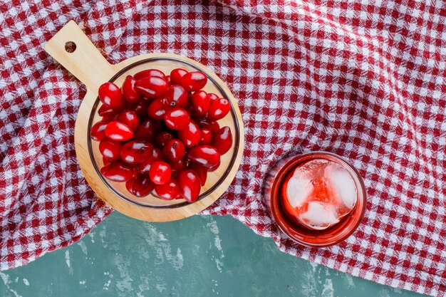 Bacche di corniolo in una ciotola con bevanda, tagliere su intonaco e panno da picnic