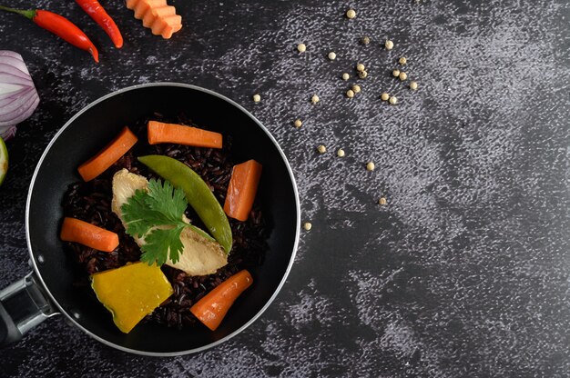 Bacche di riso viola cotte con petto di pollo grigliato. Zucca, carote e foglie di menta in padelle.