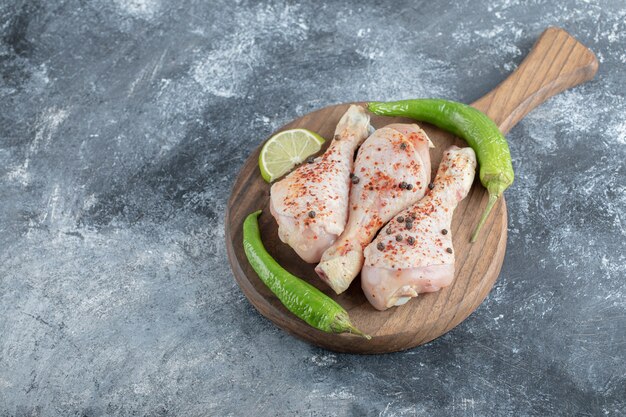 Bacchette di pollo crudo biologico fresco sul tagliere di legno su sfondo grigio.