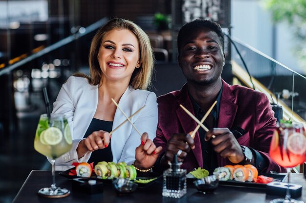 Bacchette incrociate. Due amici felici e giovani mangiano insieme i rotoli di sushi in caffè.