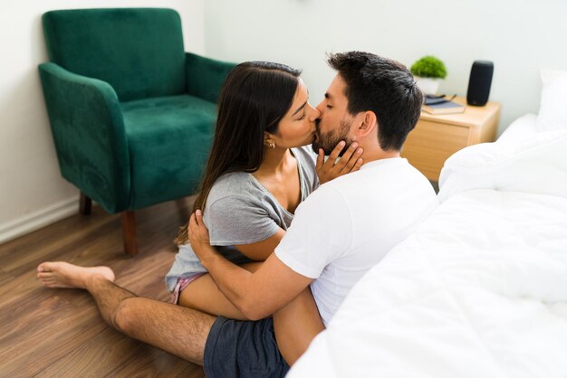 Baciarsi appassionatamente. Giovane coppia ispanica innamorata di baci e abbracci seduti sul pavimento della loro camera da letto