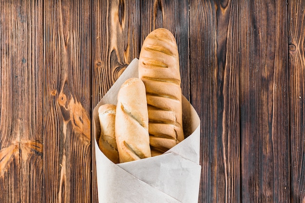 Baguette avvolto nella carta sopra il fondo in legno