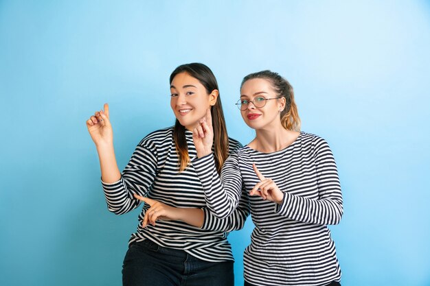 Ballando insieme. Giovani donne emotive isolate sul muro blu sfumato. Concetto di emozioni umane, esperienza facciale, amicizia, annuncio. Bellissimi modelli femminili caucasici in abiti casual.