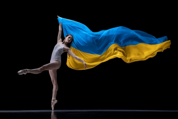 Ballerina di giovane ragazza che balla con un panno dipinto nei colori blu e gialli della bandiera dell'Ucraina su sfondo scuro per studio