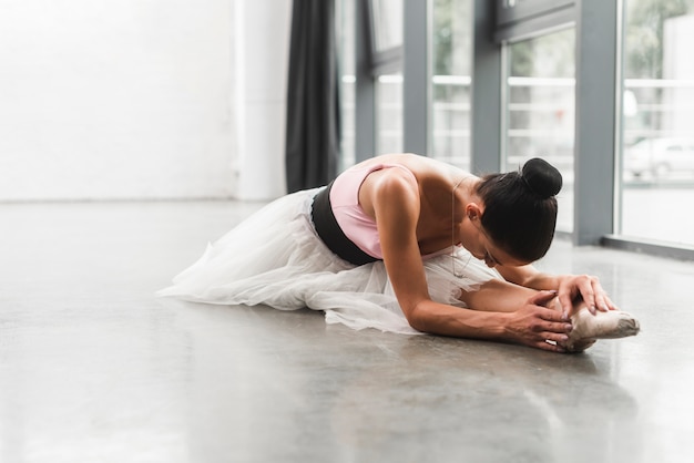 Ballerina femminile che si siede sull&#39;allungamento del pavimento