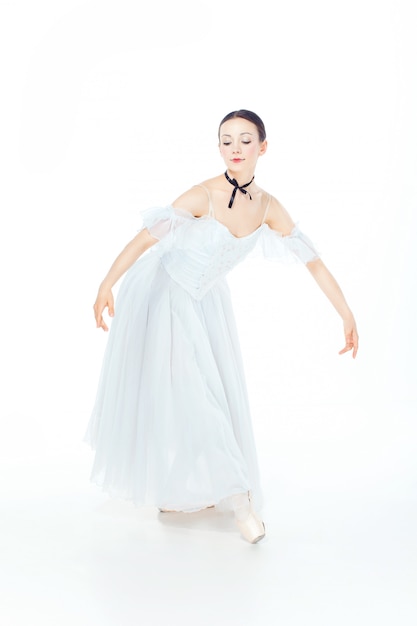 Ballerina in vestito bianco che posa sulle scarpe del pointe, bianco dello studio.