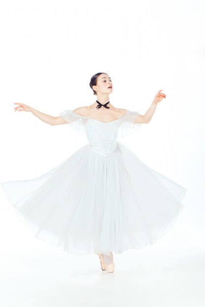 Ballerina in vestito bianco che posa sulle scarpe del pointe, fondo dello studio.