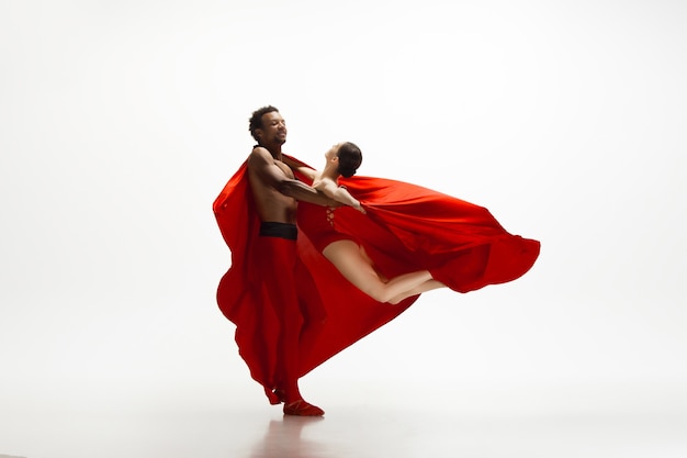 Ballerini di balletto classico grazioso che ballano isolati su priorità bassa bianca dello studio. Coppia in abiti rosso vivo come una combinazione di vino e latte. La grazia, l'artista, il movimento, l'azione e il concetto di movimento.