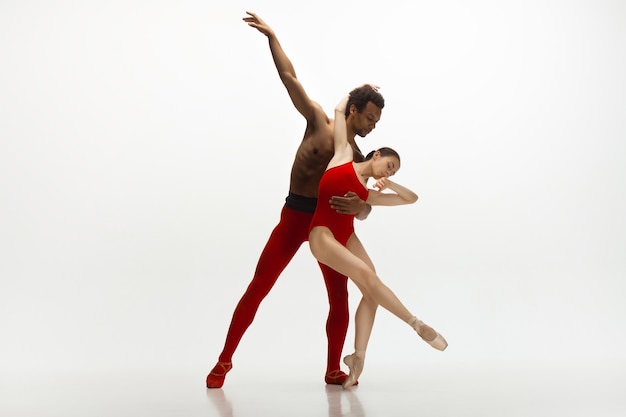 Ballerini di balletto classico grazioso che ballano isolati su priorità bassa bianca dello studio. Coppia in abiti rosso vivo come una combinazione di vino e latte. La grazia, l'artista, il movimento, l'azione e il concetto di movimento.