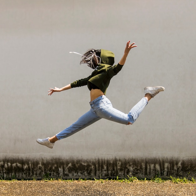 Ballerino femminile in cappa che salta contro il muro