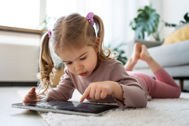 Bambina a tutto campo con tablet sul pavimento