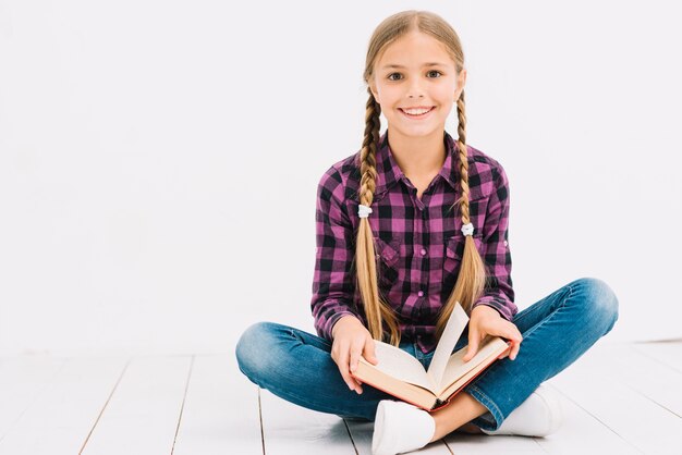 Bambina adorabile che legge un libro che si siede sul pavimento