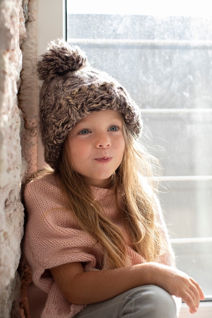 Bambina alla moda che posa con il cappello di inverno