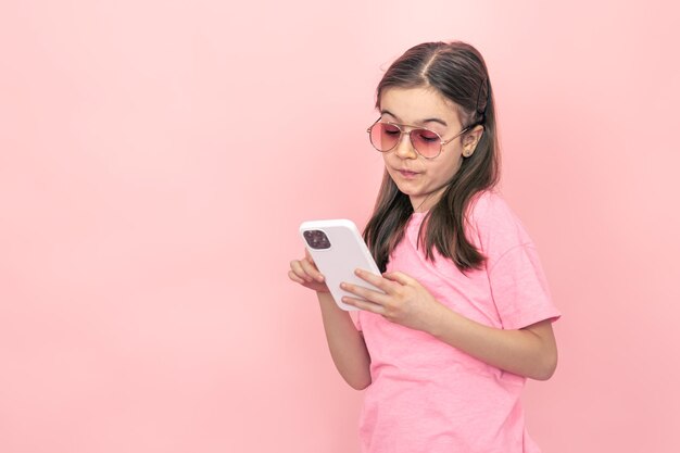 Bambina alla moda con uno smartphone su sfondo rosa