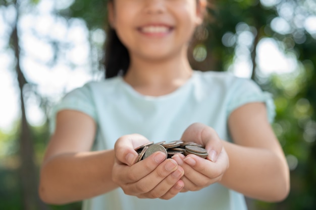 Bambina asiatica sveglia che gioca con i soldi delle monete, soldi della tenuta della mano del bambino. bambino che risparmia denaro nel salvadanaio. bambino che conta le sue monete salvate, bambini che imparano per il concetto futuro.