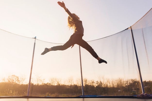 Bambina attiva che salta sopra il trampolino contro il cielo