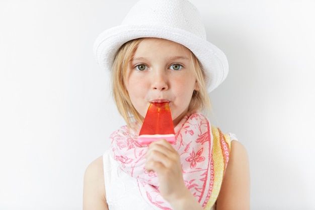 Bambina bionda che indossa cappello bianco e mangia il gelato