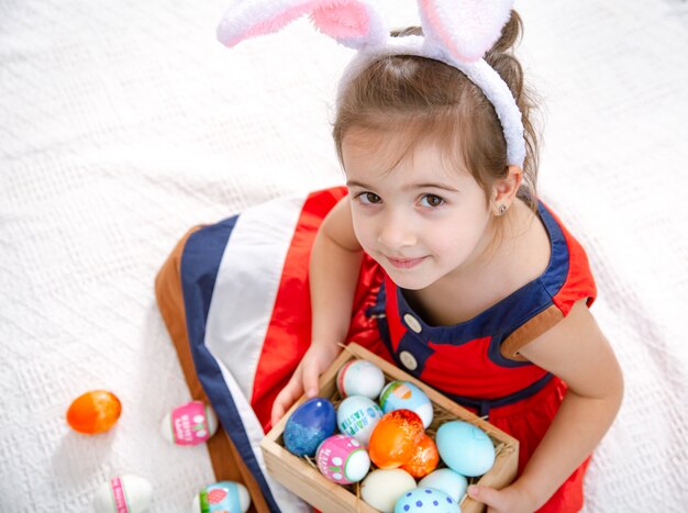 Bambina carina con uova di Pasqua e orecchie da coniglio in un bellissimo vestito luminoso.